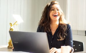 A woman laughing while sitting at a desk in front of a computer 